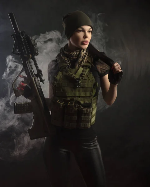 girl in military special clothes posing with a gun in his hands on a dark background in the haze