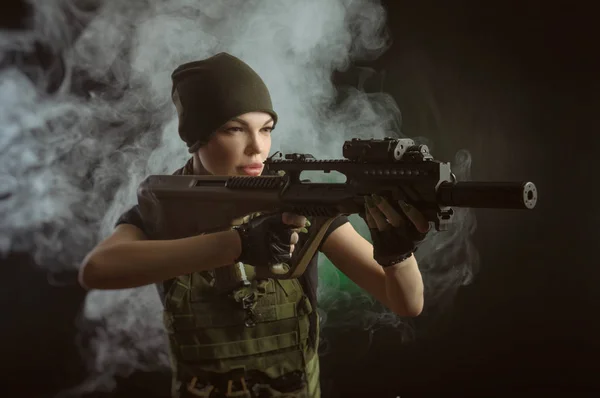 girl in military special clothes posing with a gun in his hands on a dark background in the haze