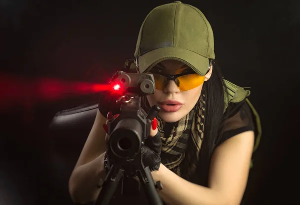 ヘイズの暗い背景の上に手で銃を持つポーズ軍の特別な服の女の子 — ストック写真