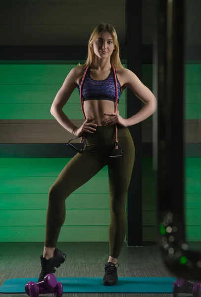 Sportliche schlanke Mädchen posiert in der Turnhalle in schöner Sportbekleidung mit Gummiband für Fitness — Stockfoto