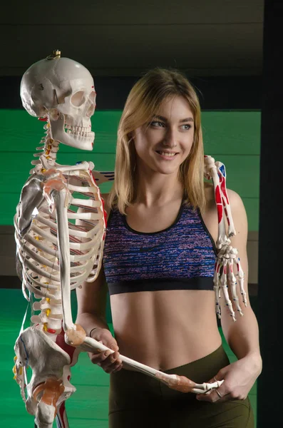 Sportlich schöne Mädchen umarmt mit einem Skelett in der Turnhalle und lacht — Stockfoto
