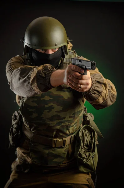 Um homem de uniforme com uma arma posando, apontando, recarregando, atirando, em um fundo escuro no estúdio — Fotografia de Stock