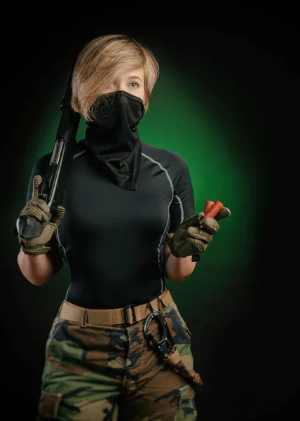 En flicka i uniform med en pistol poserar, siktar, omlastning, skytte, på en mörk bakgrund i studion — Stockfoto