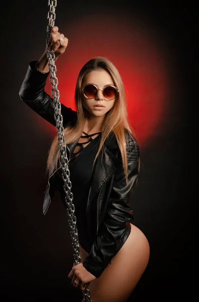 Красивая стильная модная девушка в боди-костюме в кожаных куртках позирует на фото Студия на темном фоне с цепями — стоковое фото