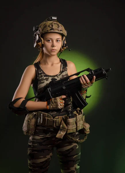 The girl in military airsoft clothes poses with a gun in her hands on a dark background — Stock Photo, Image