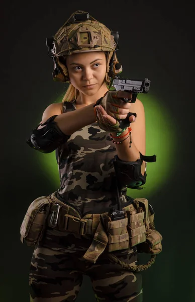 La chica con ropa militar airsoft posa con una pistola en sus manos sobre un fondo oscuro —  Fotos de Stock