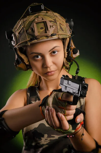 A menina em roupas militares airsoft posa com uma arma em suas mãos em um fundo escuro — Fotografia de Stock