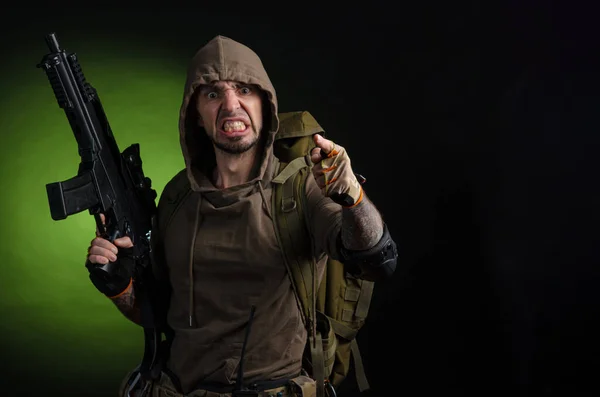 Mann Stalker mit einer Waffe mit optischem Visier und einem Rucksack auf dunklem Hintergrund mit Emotionen, die schauen, zielen, beobachten, schleichen — Stockfoto