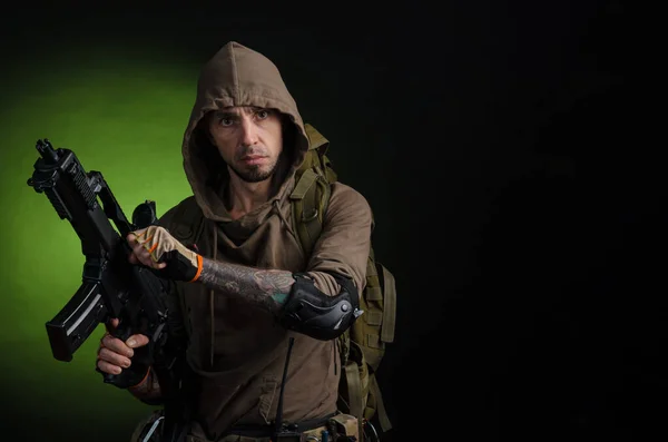 Mężczyzna Stalker z pistoletem z celownikiem optycznym i plecakiem na ciemnym tle z emocjami patrząc, celując, obserwując, skradając — Zdjęcie stockowe