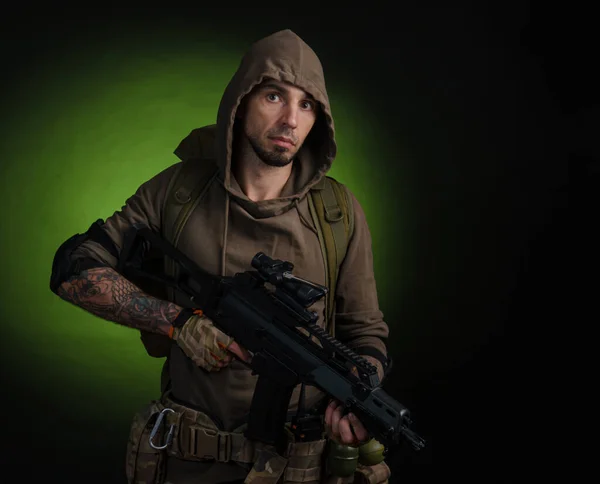 Mann Stalker mit einer Waffe mit optischem Visier und einem Rucksack auf dunklem Hintergrund mit Emotionen, die schauen, zielen, beobachten, schleichen — Stockfoto
