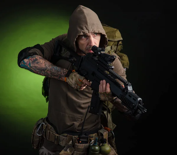 Homem perseguidor com uma arma com uma visão óptica e uma mochila em um fundo escuro — Fotografia de Stock