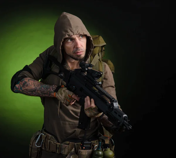 Man Stalker with a gun with an optical sight and a backpack on a dark background — Stock Photo, Image