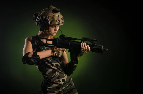 The girl in military airsoft clothes poses with a gun in her hands on a dark background — Stock Photo, Image