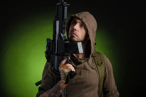Homem perseguidor com uma arma com uma visão óptica e uma mochila em um fundo escuro — Fotografia de Stock