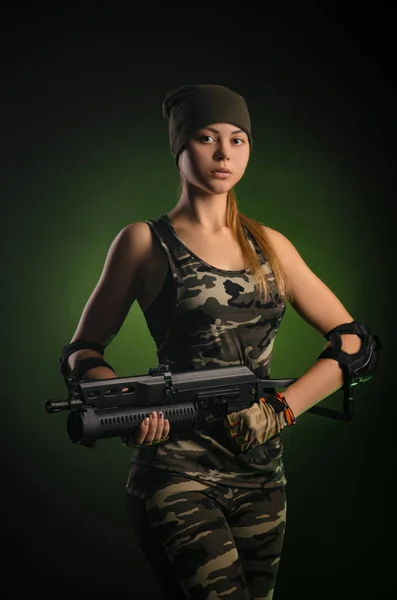 Das Mädchen in militärischen Overalls luftweich posiert mit einem Gewehr in den Händen vor dunklem Hintergrund im Dunst — Stockfoto