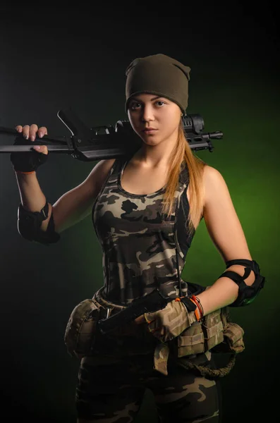La ragazza in tuta militare airsoft posa con una pistola tra le mani su uno sfondo scuro nella foschia — Foto Stock