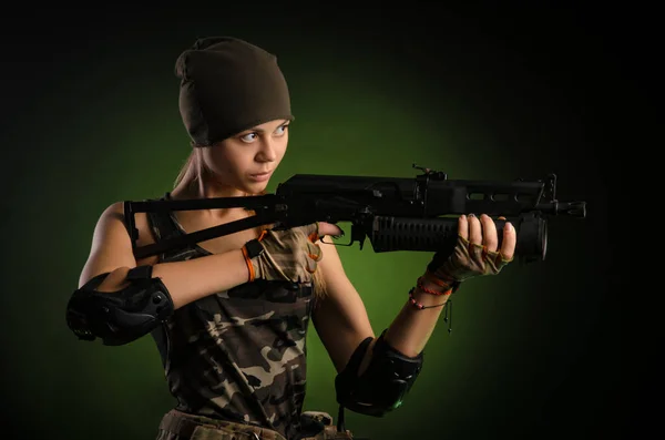 Das Mädchen in militärischen Overalls luftweich posiert mit einem Gewehr in den Händen vor dunklem Hintergrund im Dunst — Stockfoto