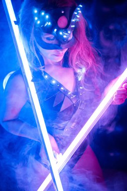 Seksi kedi ve parti kostümlü bir kız Cadılar Bayramı için neon bir sette poz veriyor.