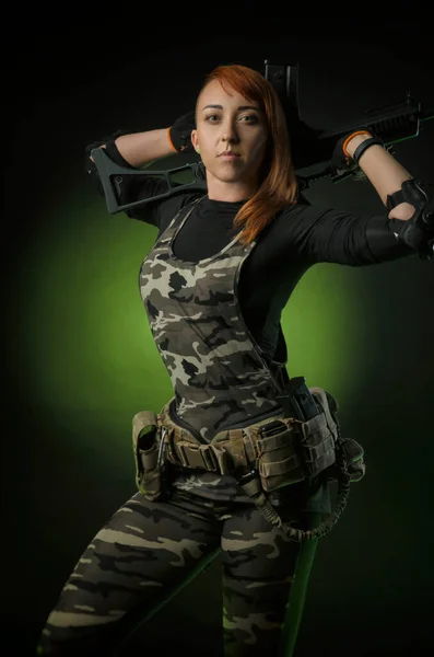 Flickan i militära airsoft kläder poserar med en pistol i händerna på en mörk bakgrund — Stockfoto