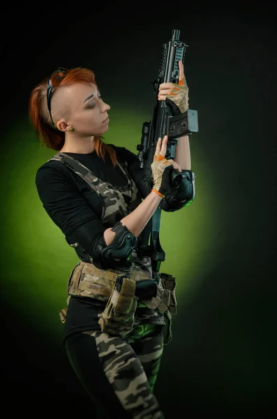 The girl in military airsoft clothes poses with a gun in her hands on a dark background — Stock Photo, Image