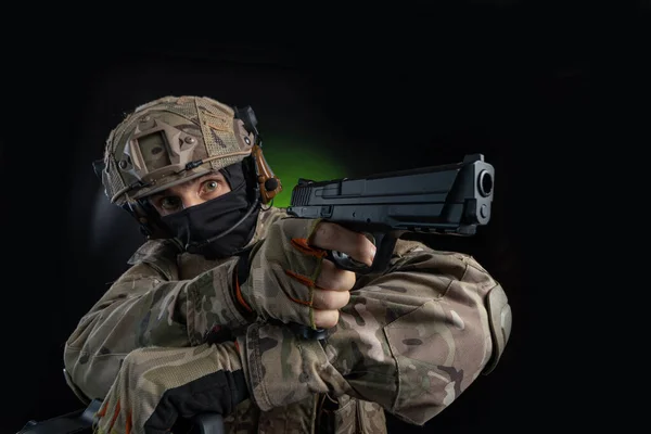 En manlig soldat i militära kläder med ett vapen på en mörk bakgrund — Stockfoto