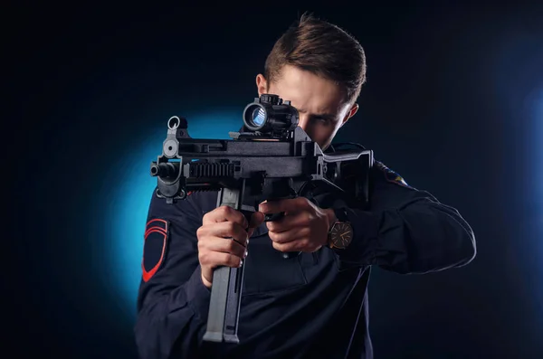 Um cara de uniforme de polícia com uma espingarda automática de cano curto com uma visão telescópica mira — Fotografia de Stock