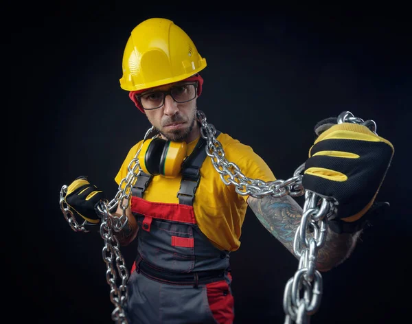 Een man in een constructie reparateurs overall houdt een metalen ketting in zijn handen — Stockfoto