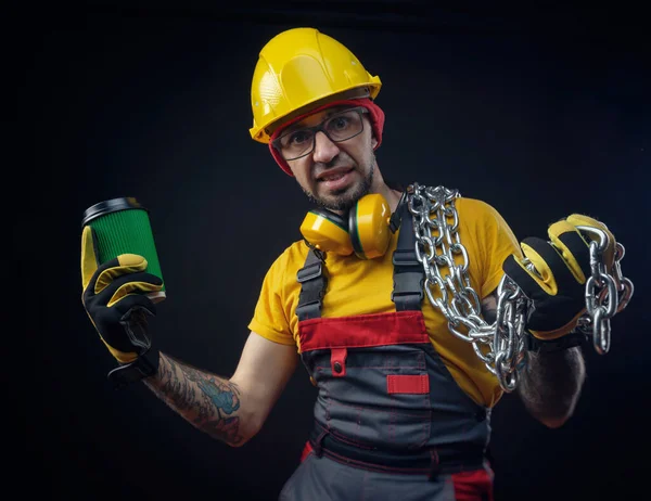 Een man in een constructie reparaties jumpsuit met een metalen ketting en een koffie Cup — Stockfoto