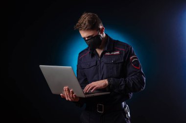 Yüzünde dizüstü bilgisayar ve sağlık maskesi olan polis üniformalı yakışıklı bir adam. Polisin İngilizce çevirisi 