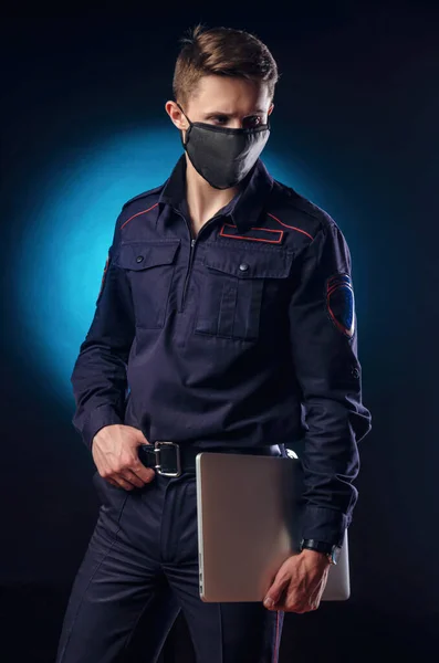 Красивый парень в полицейской форме с ноутбуком на лице и медицинской маской  . — стоковое фото