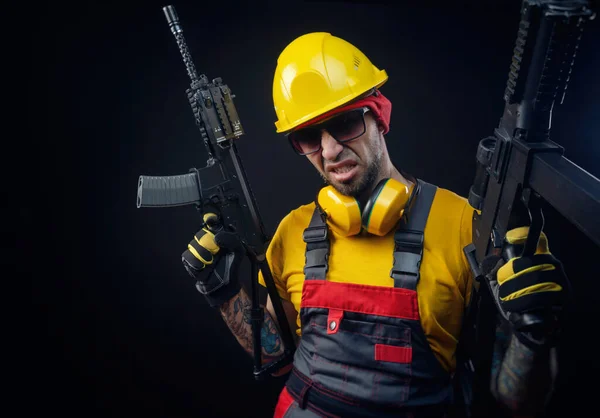 Mężczyzna w mundurze robotnika budowlanego noszący twardy kapelusz z airsoftową bronią w rękach — Zdjęcie stockowe