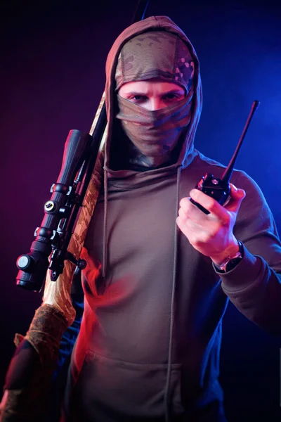 Um cara em um Balaclava com um rifle sniper na luz do néon — Fotografia de Stock