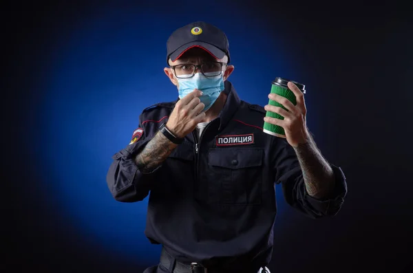 De man in het politie-uniform is een Russische politieagent met een medisch masker met een koffiebeker in zijn hand. Engelse vertaling van "Police" — Stockfoto