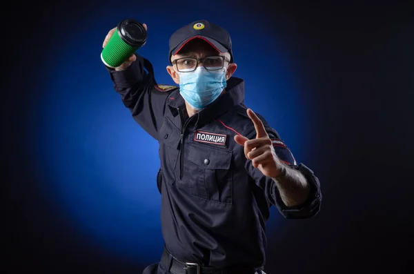 警察の制服の男はロシアの警察官です医療用マスクにコーヒーカップを手にしています。日本語訳「警察」" — ストック写真