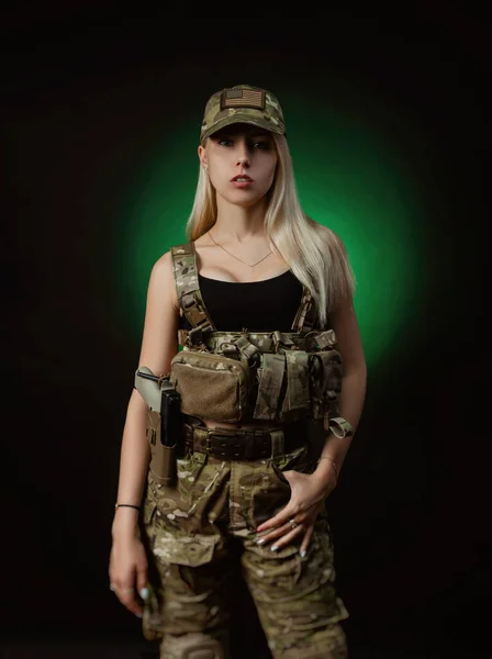 Een sexy meisje in militaire airsoft overalls poses met een pistool in haar handen op een donkere achtergrond — Stockfoto