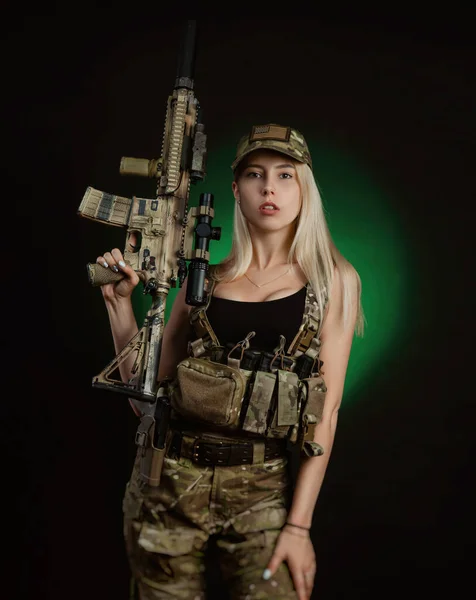 Una chica sexy en overoles militares airsoft posa con una pistola en sus manos sobre un fondo oscuro — Foto de Stock