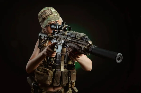 Una chica sexy en overoles militares airsoft posa con una pistola en sus manos sobre un fondo oscuro —  Fotos de Stock