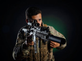 egy brutális fickó katonai airsoft overálban, fegyverrel a kezében egy sötét háttérben.