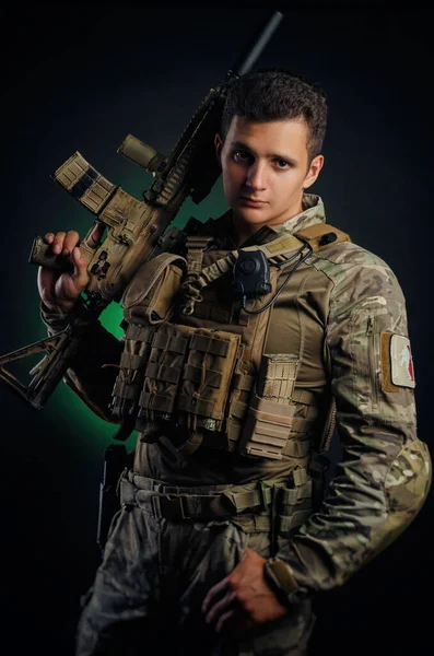 Brutální chlap ve vojenských airsoftových kombinézách pózuje se zbraní v rukou na tmavém pozadí — Stock fotografie