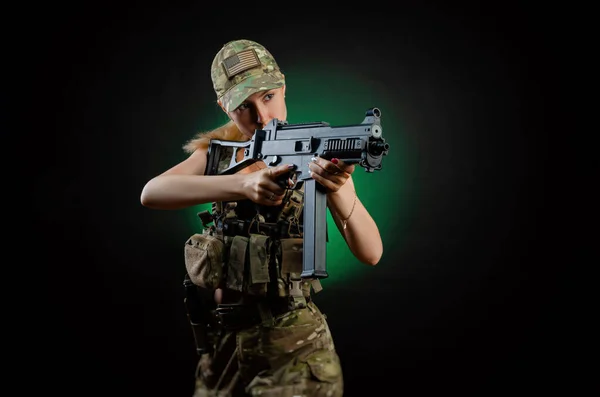 Uma menina sexy no macacão airsoft militar posa com um rifle de assalto em um fundo escuro — Fotografia de Stock