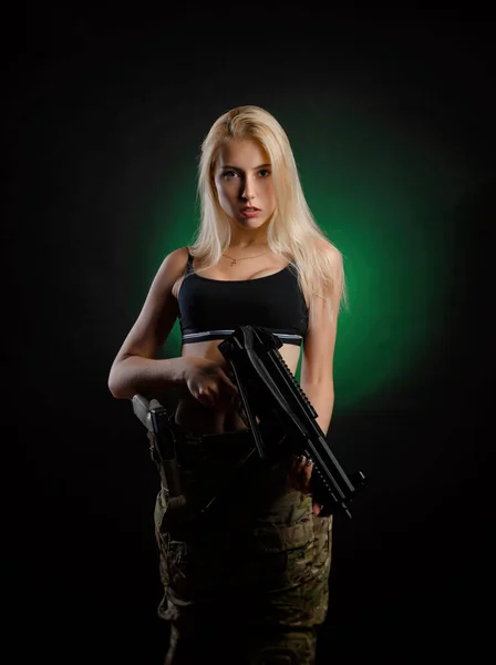 Askeri hava yumuşaklığında seksi bir kız siyah arka planda bir saldırı tüfeğiyle poz veriyor. — Stok fotoğraf