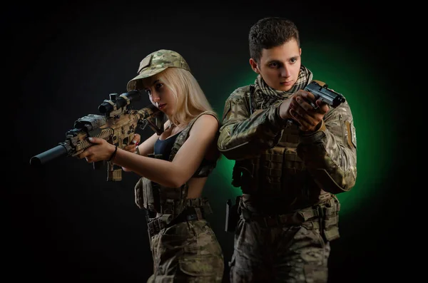 Una chica y un tipo en mono militar posan con una pistola de airsoft sobre un fondo oscuro —  Fotos de Stock