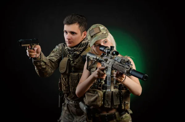 Uma menina e um cara em macacão militar posar com uma arma airsoft em um fundo escuro — Fotografia de Stock