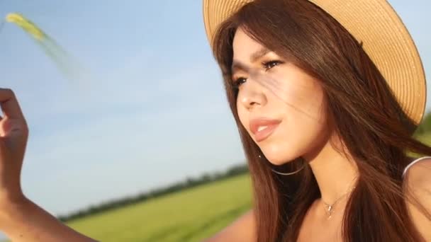 Dívka v krásných letních šatech a klobouku na pšeničném poli drží hřeby — Stock video