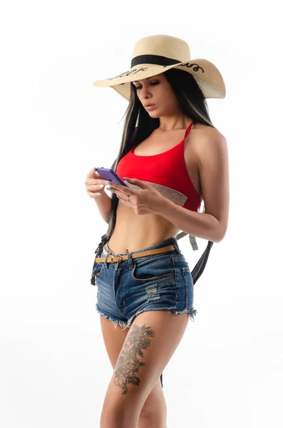 Брюнетка в шляпе в летней одежде стройная и сексуальная с телефоном на белом фоне — стоковое фото