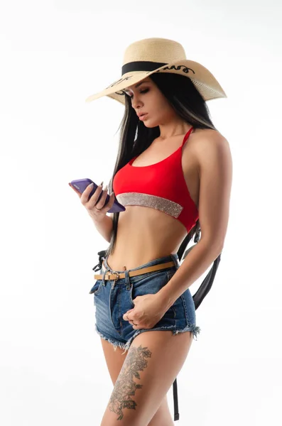 Brunette dans un chapeau en vêtements d'été mince et sexy avec un téléphone isolé sur un fond blanc — Photo