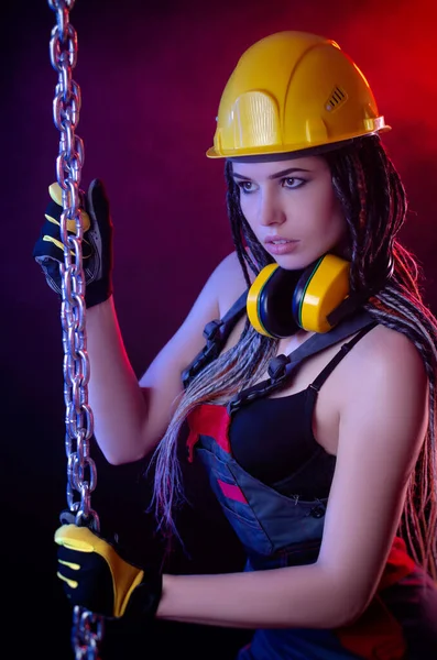 Een bouwmeisje met een harde hoed en overalls met een lange ketting in haar handen — Stockfoto