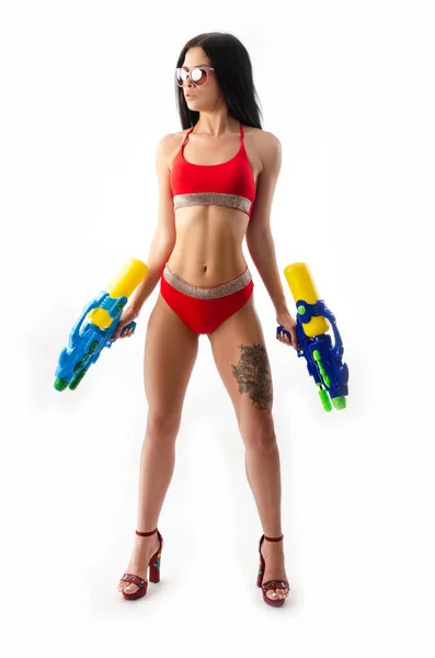 Ragazza bruna con una pistola ad acqua in costume da bagno rosso, sottile e sexy — Foto Stock