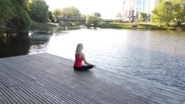 Kız gün doğumunda nehir kenarındaki iskelede meditasyon yapıyor.