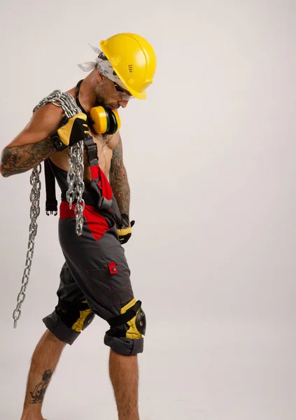 Un hombre en un mono reparador de la construcción sostiene una cadena de metal en sus manos — Foto de Stock